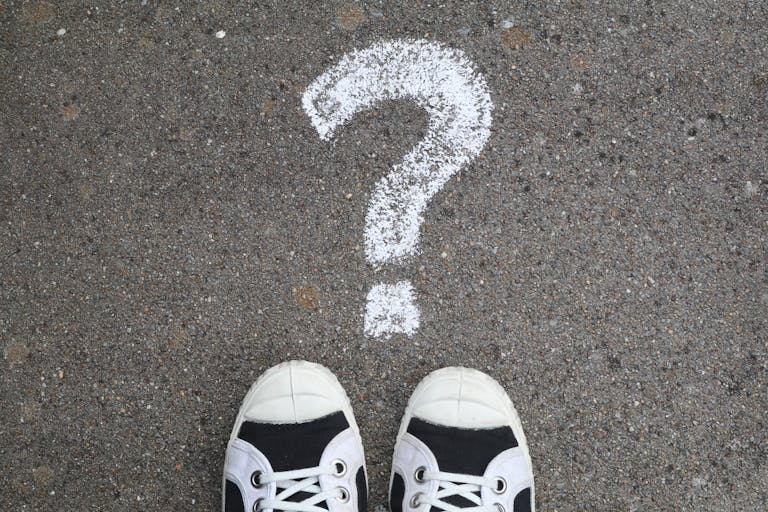 Sneakers on pavement with a chalk question mark, symbolizing curiosity or decisions.