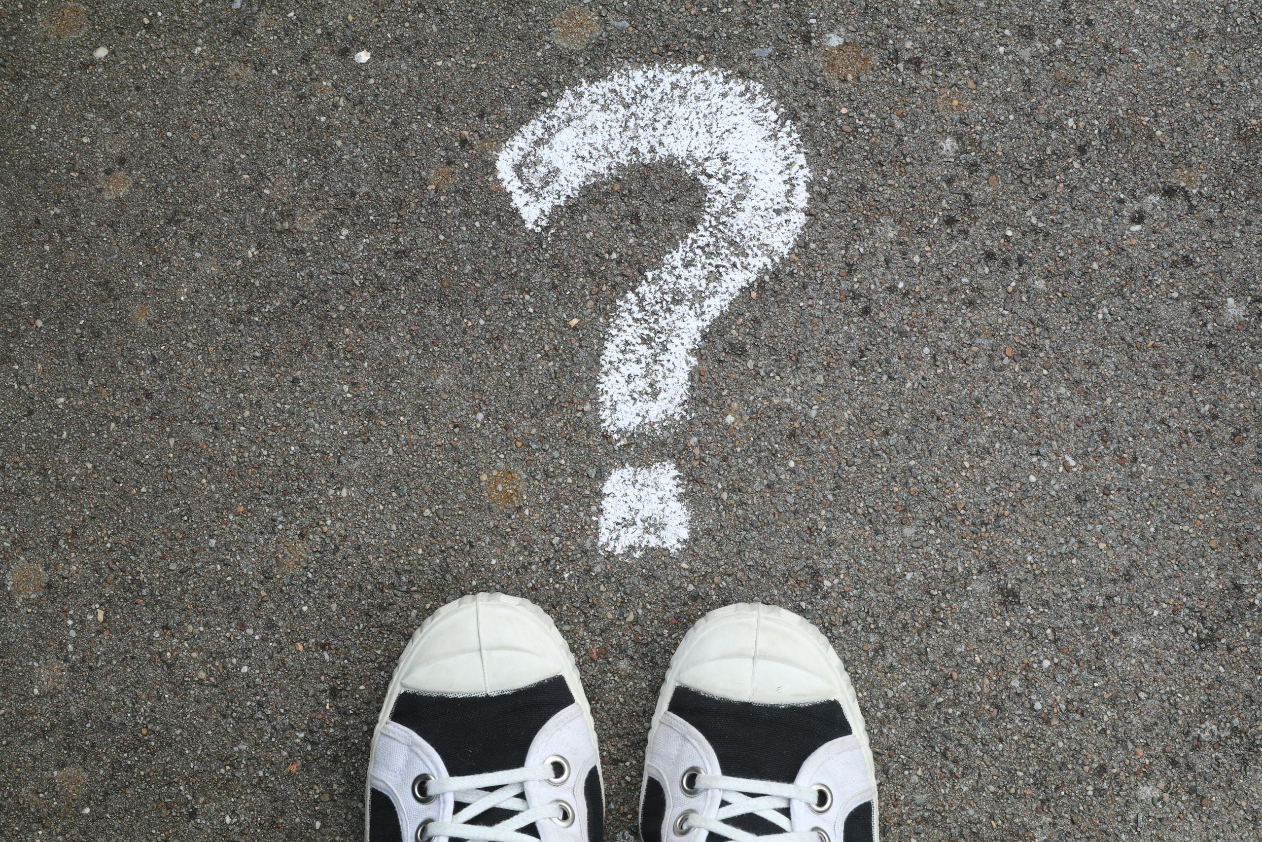 Sneakers on pavement with a chalk question mark, symbolizing curiosity or decisions.