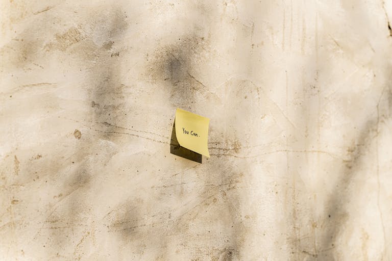 A yellow sticky note with 'You Can' written, placed on a textured outdoor wall.